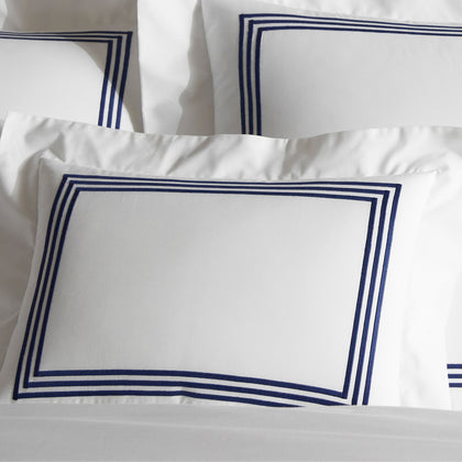 Close-up of stacked white BelTempo pillow shams with triple navy line embroidered borders.