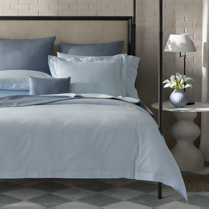 Pale blue Bel Tempo Nocturne bedding with slate quilted pillows, styled on a four-poster bed.
