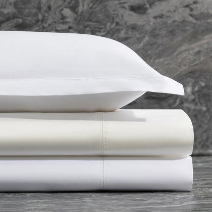 Stacked white Bergamo Hemstitch sheets with hemstitch trim against a marble backdrop.