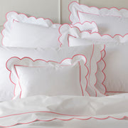White bedding with a scalloped pink embroidered border, pillow shams layered together.