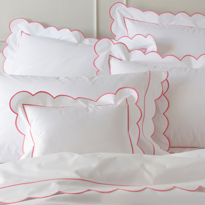 White bedding with a scalloped pink embroidered border, pillow shams layered together.