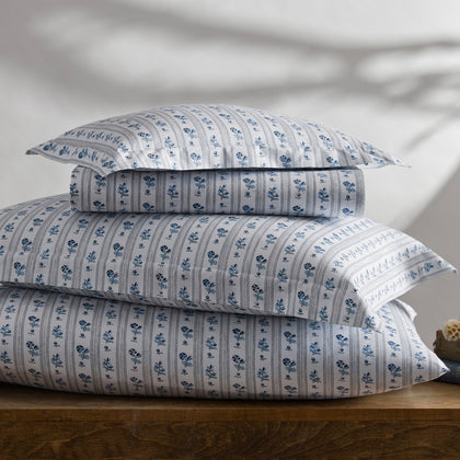 Blue and white Cabanon Stripe floral bedding stacked on a wooden table.