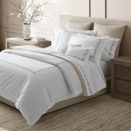 White Callista bedding with lavender floral embroidered border, styled on a bed with a flowering branch.