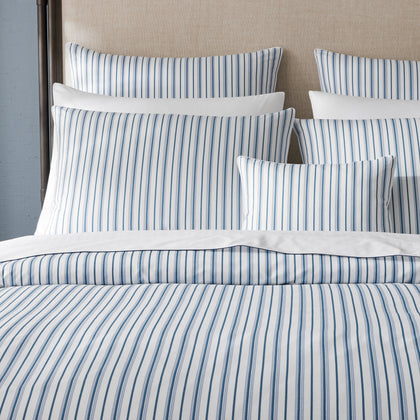 Blue and white striped Calypso bedding styled on a bed with an upholstered headboard.