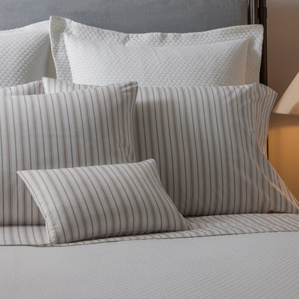 Calypso tan striped pillows layered with white textured shams on bed.