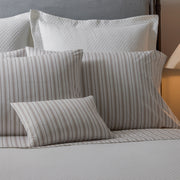 Calypso tan striped pillows layered with white textured shams on bed.