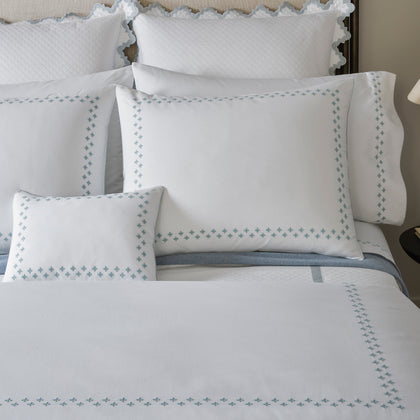 Casablanca white bedding with blue embroidered trellis border styled on a bed.