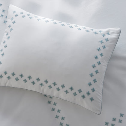 Casablanca white pillow with blue embroidered border styled on a bed.