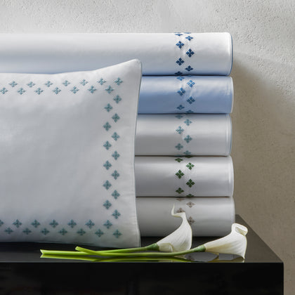 Casablanca embroidered sheets stacked in blue tones beside calla lilies