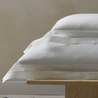 White Cecily pillows with lattice lace trim, stacked on a stone bench.