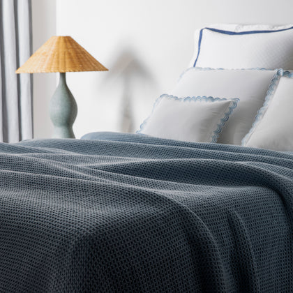 Navy waffle-weave Chatham blanket draped on a bed with scalloped blue-trimmed shams.
