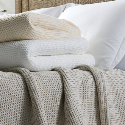 Waffle-weave Chatham blankets in tan, ivory, and white, folded and draped on a bed.