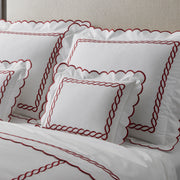 White bedding with a red chain-link embroidered border and scalloped edge, upholstered headboard.