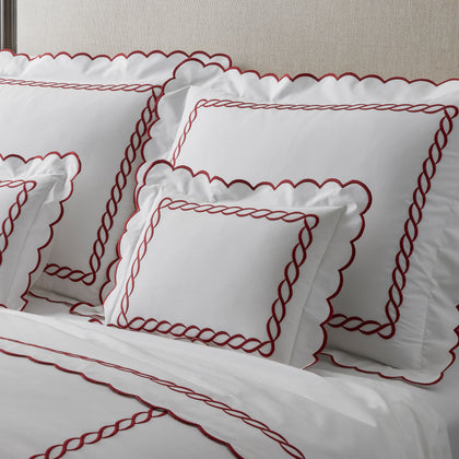 White bedding with a red chain-link embroidered border and scalloped edge, upholstered headboard.