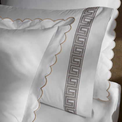White pillow shams with a tan scalloped edge, white sheet with a brown Greek-key embroidered border.