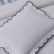 White pillow sham with a navy scalloped edge, blue ikat-print fabric visible in the corner.