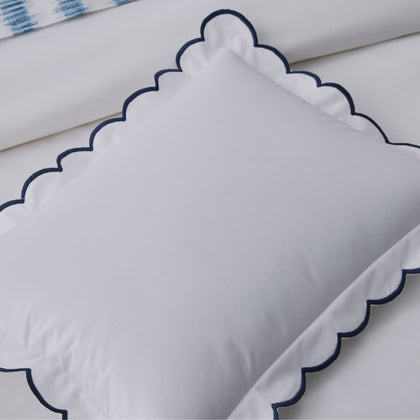 White pillow sham with a navy scalloped edge, blue ikat-print fabric visible in the corner.