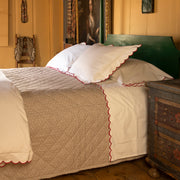 White bedding with a red scalloped edge, tan patterned quilted coverlet, green painted wood headboard, antique chest, portrait painting.