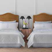 Twin rattan beds with white bedding, blue scalloped edge, striped pillow shams with "O" and "G" monograms, tulips on a nightstand.
