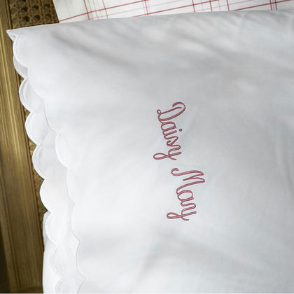 White pillow sham with a scalloped edge, embroidered "Daisy May" in pink script.