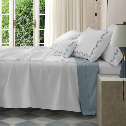 White Daphne Matelasse quilted bedding with blue floral embroidery, styled on a bed near French doors.