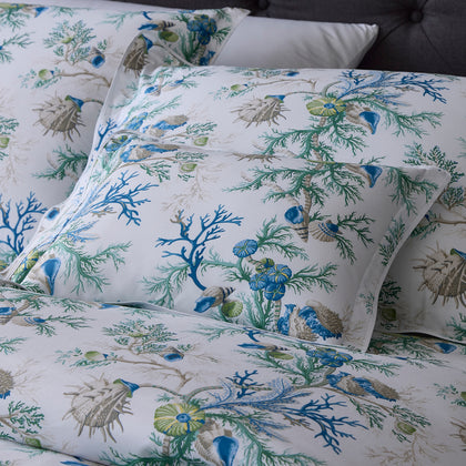 Close-up of blue Del Tesoro coral and shell print pillows against a dark tufted headboard.