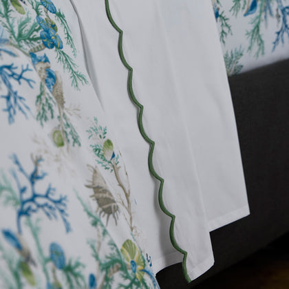 Close-up of blue Del Tesoro coral print bedding next to white sheets with a green scalloped trim.
