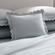 Pale blue Diamond Pique sham with scalloped trim on a bed.