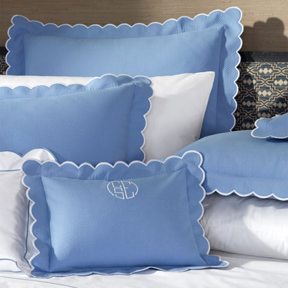Close-up of blue DiamondPique pillow shams with scalloped white edges, one embroidered with a monogram.