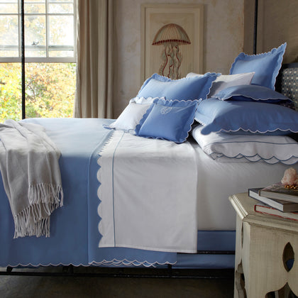 Bed dressed in blue DiamondPique bedding with white scalloped trim, on an iron bed frame below a jellyfish illustration, with a gray throw.