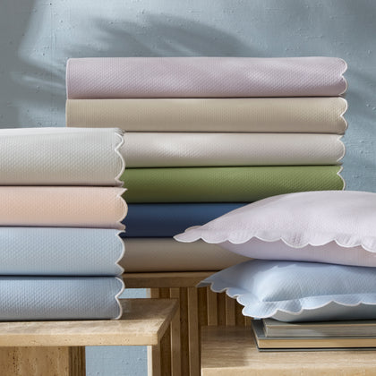 Diamond Pique scalloped sheets in pastel colors, stacked with matching pillows on side tables.
