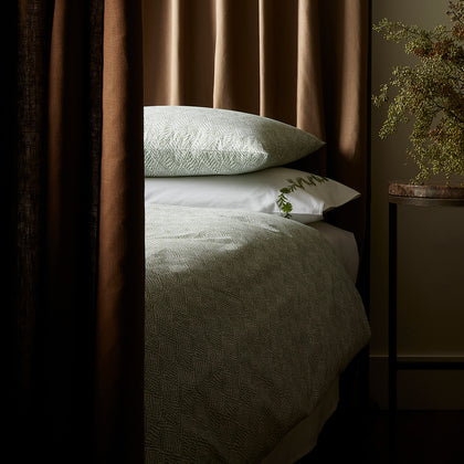 Green diamond-print Duma Diamond bedding styled on a curtained canopy bed in dim light.
