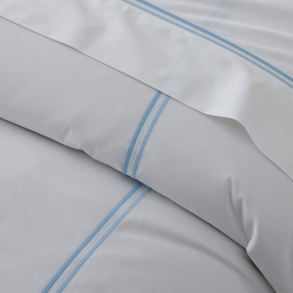Close-up of folded white Essex sheets with a double-line blue embroidered border.