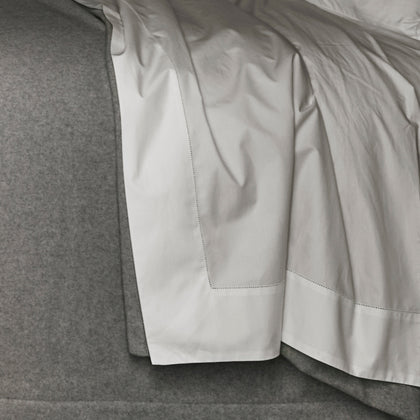Gatsby white percale sheet with a hemstitch border, draped on a headboard