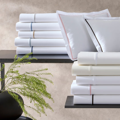 White Gatsby sheets with single-stripe trim, stacked beside pink and black-bordered shams.