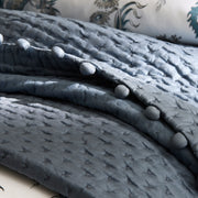 Close-up of a slate-blue smocked coverlet with fabric-covered buttons