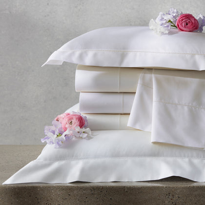 Ivory Gatsby Hemstitch sheets stacked with pink and lavender flowers.