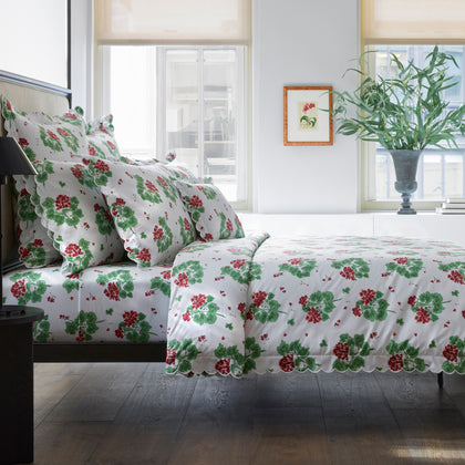Red and green Geranium floral bedding styled on a dark wood bed by windows.