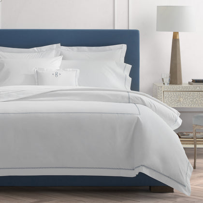 White Hatch bedding with navy cross-stitch trim, styled on a blue upholstered bed.