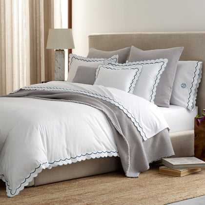 White India scalloped bedding with blue trim, styled on a bed with a gray throw.