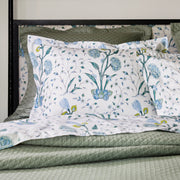 Blue floral Khilana shams layered over a sage green quilted coverlet, on a black iron headboard.