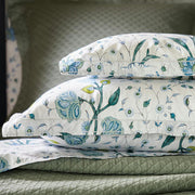Close-up of stacked blue floral Khilana pillow shams over a sage green quilted coverlet.