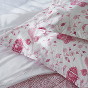 Close-up of pink floral quilted pillow shams beside a white scalloped pillowcase and a pink dotted sheet.