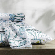 Draped blue floral Khilana sheet and pillow sham on a stone surface, with leafy shadows on the wall behind.