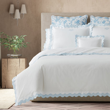 White Lorelei scalloped bedding with light blue trim, styled on a bed with floral shams.