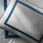 Close-up of a white Louise pillow with blue ribbon trim, on matching sheets.