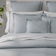 Gray diamond-patterned bedding with white piped pillows, styled on a bed with a white headboard and a plant beside it.