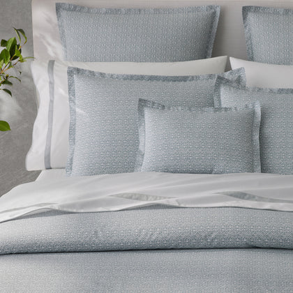 Gray diamond-patterned bedding with white piped pillows, styled on a bed with a white headboard and a plant beside it.