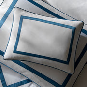 Overhead view of a white Louise pillow with blue ribbon trim, on matching sheets.