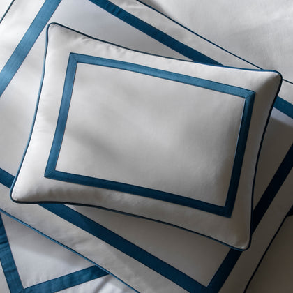 Overhead view of a white Louise pillow with blue ribbon trim, on matching sheets.